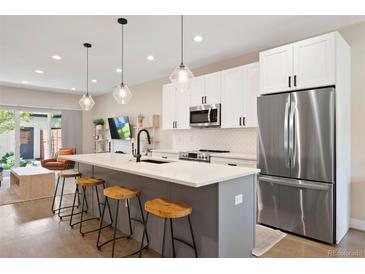 Modern kitchen boasts stainless appliances, white cabinets, island with seating, and stylish pendant lighting at 3103 S Cherokee St, Englewood, CO 80110