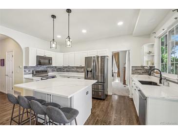 Bright kitchen features a large center island with marble countertops, stainless steel appliances, and pendant lighting at 7513 Simms Ct, Arvada, CO 80005