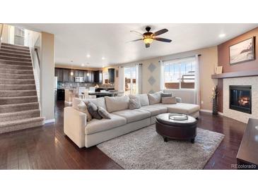 Bright, open-concept living room with a fireplace, hardwood floors, a large sectional, and modern kitchen in background at 3140 S Nepal Way, Aurora, CO 80013