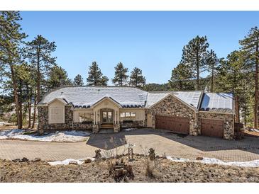 Charming stone home with a driveway that leads to a three-car garage, nestled amongst mature trees, with a roof dusted in snow at 24860 N Mountain Park Dr, Evergreen, CO 80439