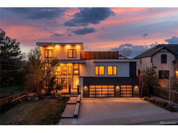 Stunning modern home featuring a sleek design, three-car garage, and beautiful landscaping against a colorful sunset backdrop at 942 S Fulton St, Denver, CO 80247