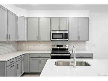 Modern kitchen featuring gray cabinets, stainless steel appliances, and white quartz countertops at 17115 W 91St Ln, Arvada, CO 80007