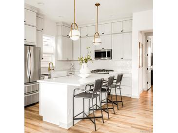 Bright kitchen features white cabinets, stainless appliances, a kitchen island with bar stool seating and modern pendant lights at 1925 W 165Th Way, Broomfield, CO 80023