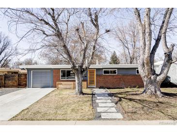 Charming single-story home featuring a brick facade, gray trim, mature trees, and a well-manicured lawn with concrete stepping stones at 5945 Dudley Ct, Arvada, CO 80004