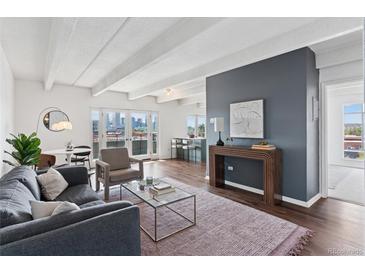 Bright living room features exposed beams, hardwood floors, and floor to ceiling sliding glass doors with city views at 1441 N Humboldt St # 505, Denver, CO 80218