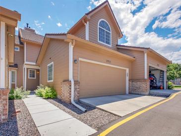 Inviting tan two-story townhome featuring a two-car garage and walkway with lovely landscaping at 5976 S Jellison St # E, Littleton, CO 80123