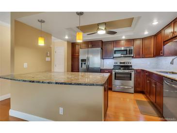 A well-lit kitchen featuring stainless steel appliances, wooden cabinetry, granite countertops, and a breakfast bar at 13961 E Marina Dr # 314, Aurora, CO 80014