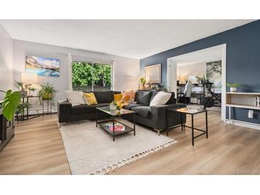 Bright living room featuring neutral and navy walls, wood flooring, and a sliding glass door to the balcony at 7040 E Girard Ave # 207, Denver, CO 80224