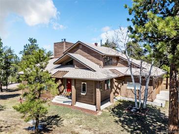 Inviting two-story home featuring wood siding, multiple gables, mature trees, and a bright red front door at 18940 Pebble Beach Way, Monument, CO 80132