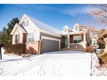 Charming two-story home featuring brick accents, a welcoming front porch, gray siding, and a gray two car garage at 8387 Fig St, Arvada, CO 80005