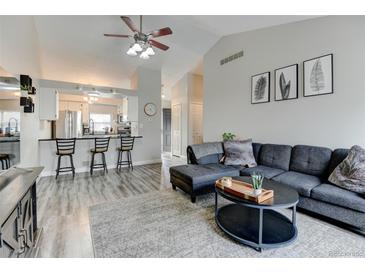 Open-concept living room featuring a gray sofa, vaulted ceilings, and a breakfast bar overlooking the kitchen at 4108 S Rifle Way, Aurora, CO 80013