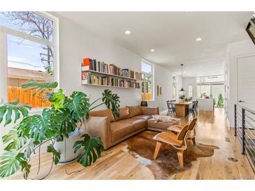Bright living room features a brown leather sofa, hardwood floors, and stylish decor with a view into the open concept dining area at 1833 E Jewell Ave, Denver, CO 80210