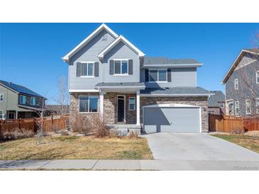 Charming two-story home featuring a stone facade, gray siding, and a two-car garage, set against a clear blue sky at 19603 E 63Rd Pl, Aurora, CO 80019
