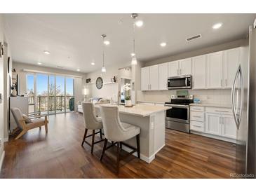 Bright open kitchen features white cabinets, stainless appliances, and a spacious island with seating at 400 E Fremont Pl # 205, Littleton, CO 80122