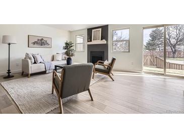 Bright living room with light wood floors, fireplace, neutral furnishings, and large windows at 11981 E Yale Ave, Aurora, CO 80014
