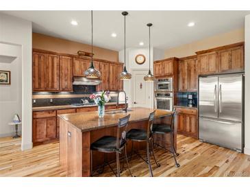 Modern kitchen with a large central island, wood cabinets, stainless steel appliances, and stylish pendant lighting at 2714 Calmante Pl, Superior, CO 80027