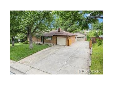 Brick home featuring a large concrete driveway and mature trees providing shade and curb appeal at 1475 S Urban Way, Lakewood, CO 80228