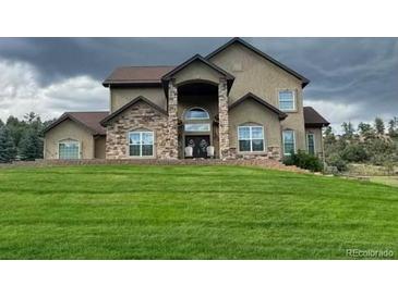 Stunning two-story home featuring a beautiful stone entrance and a lush green front lawn at 4619 Mohawk Dr, Larkspur, CO 80118