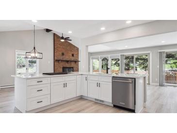 Bright kitchen boasts white cabinetry, quartz countertops, stainless steel appliances, and a brick fireplace feature at 10506 Brown Fox Trl, Littleton, CO 80125