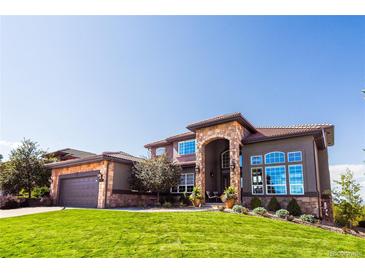 Stunning two-story home featuring stone accents, a well-manicured lawn, and a grand arched entryway at 12457 Topaz Vista Way, Castle Pines, CO 80108