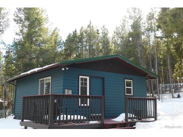 Quaint blue cabin with a deck, nestled in a snowy forest setting at 28 Deer Rd, Evergreen, CO 80439
