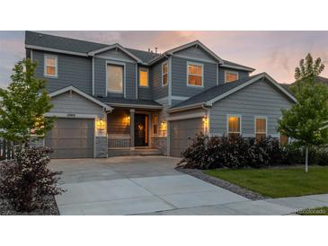Inviting gray two-story home boasts a three-car garage, manicured landscaping, and a welcoming front porch at 12953 Bridge View Ln, Parker, CO 80134