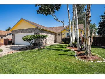 Charming yellow and brick home with a well-manicured lawn and mature trees enhancing its curb appeal at 1030 S Fulton Ave, Fort Lupton, CO 80621
