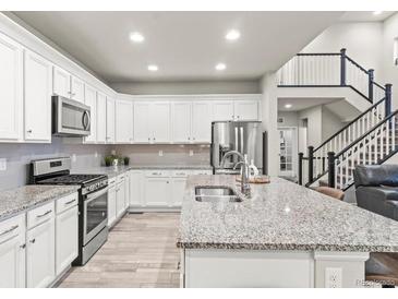 Bright kitchen features white cabinets, granite countertops, stainless steel appliances, and a spacious island at 17880 W 94Th Dr, Arvada, CO 80007