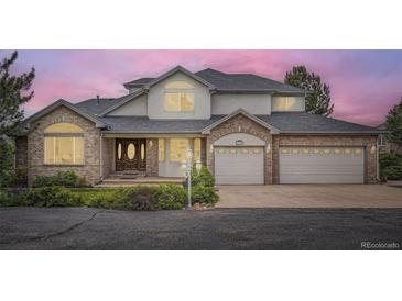 Charming two-story home with a brick facade, gray roof, lush landscaping, and a three-car garage at 6335 Oberon Rd, Arvada, CO 80004