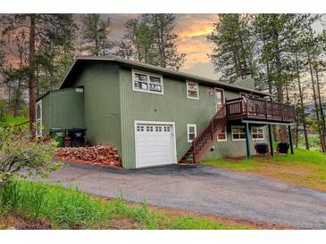 Charming green two-story home with a deck and a garage surrounded by lush trees and a driveway at 5237 S Olive Rd, Evergreen, CO 80439