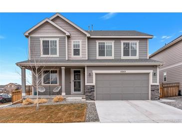 Charming two-story home with gray siding, a covered front porch, and an attached two-car garage at 5253 Cherry Blossom Dr, Brighton, CO 80601