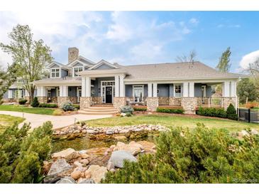 An elegant home showcasing a landscaped yard, a picturesque pond, and an inviting covered porch with stone accents at 5425 S University Blvd, Greenwood Village, CO 80121
