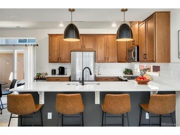 Open kitchen features a large island with seating, stainless appliances, and stylish pendant lighting at 10149 Xanadu Street, Commerce City, CO 80022