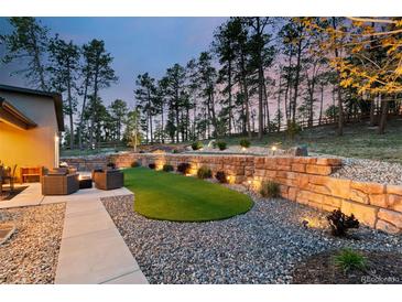 A beautifully landscaped backyard with stone retaining walls, a lush lawn area, and comfortable seating around a fire pit at 16244 Thunder Cat Way, Monument, CO 80132