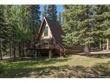 A-frame home with a brown exterior, surrounded by lush trees, featuring a wooden deck and staircase at 100 Aspen Ln, Evergreen, CO 80439