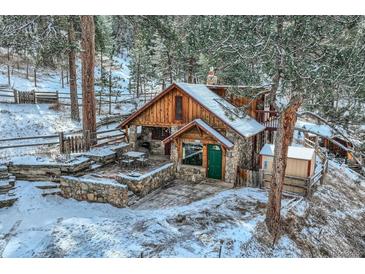 Charming wood and stone cabin with snow-covered roof and patio in a serene wooded setting at 26288 S End Rd, Kittredge, CO 80457