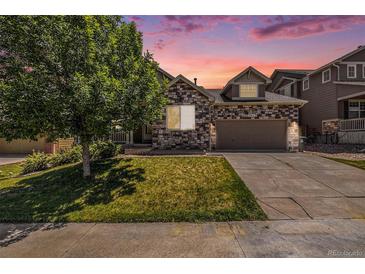 Charming home with a stone facade, well-manicured lawn, mature tree, and driveway leading to a two-car garage at 21444 E Lehigh Ave, Aurora, CO 80013