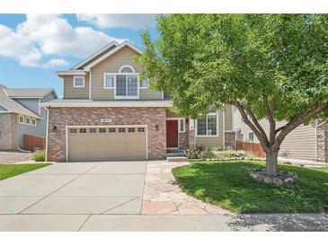 Charming two-story home featuring a red brick facade, manicured lawn, and mature shade tree at 10115 Cook St, Thornton, CO 80229