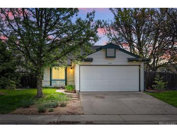 Charming single-story home with a two-car garage, green lawn, and mature trees at sunset at 2390 N Springwood Ct, Lafayette, CO 80026