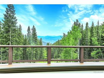 Breathtaking mountain views from a deck with brown railing, surrounded by lush green trees against a stunning blue sky at 1176 Raven Ridge Rd, Idaho Springs, CO 80452