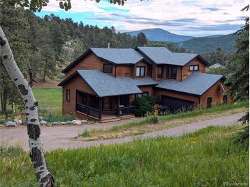 Mountain home featuring a wood exterior, gray roof, porch and garage nestled in a wooded setting with mountain views at 31299 Manitoba Dr, Evergreen, CO 80439