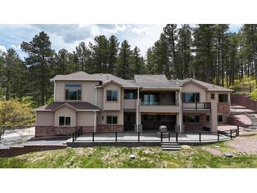 Expansive tan stucco home with stone accents, large windows, and a spacious patio area in a wooded setting at 1988 Lake Dr, Larkspur, CO 80118