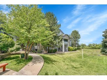 Inviting condo exterior with stone accents, a manicured lawn, mature trees, and blue sky at 8065 W Eastman Pl # 6-102, Denver, CO 80227