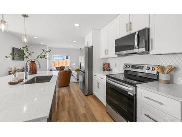 Modern kitchen with white cabinets, stainless steel appliances, and quartz countertops open to the living room at 1337 N Alton St, Aurora, CO 80010