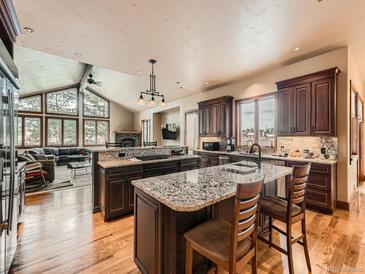 Spacious kitchen with granite countertops, wooden cabinets, island with seating, and wood flooring at 15955 W 52Nd Dr, Golden, CO 80403