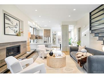 Bright, open living room with hardwood floors, a modern fireplace, and white armchairs flowing into the kitchen at 2659 S Cherokee St, Denver, CO 80223