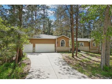 Charming ranch-style home featuring an attached two-car garage and long driveway surrounded by lush trees at 8095 Bannock Dr, Larkspur, CO 80118