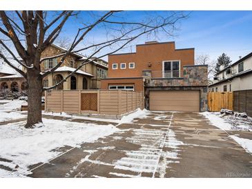 Contemporary home featuring a stone accent wall, a balcony, and a spacious driveway covered in snow at 467 Harrison St, Denver, CO 80206