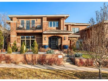 Striking two-story brick home with black iron gate, balcony, mature trees and meticulously manicured landscaping at 418 Steele St, Denver, CO 80206