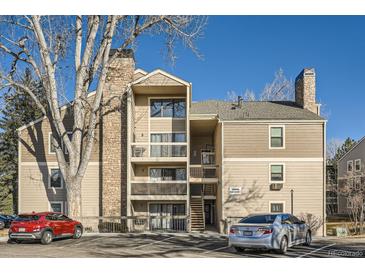 Multi-story condo building with beige siding, stone chimney, and balconies, with parking area at 4866 S Dudley St # 2, Littleton, CO 80123